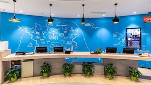 Mostrador de recepción con pared azul que muestra un mapa e iconos, una pantalla digital y plantas en macetas.