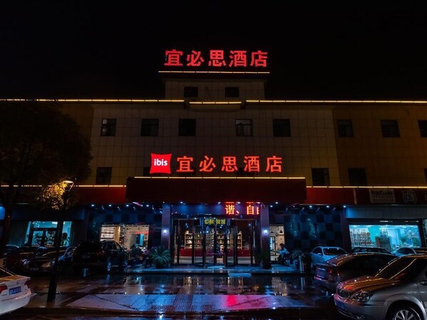 Un hôtel reconnaissable à son grand panneau rouge, à son entrée fermée par un portail et à son reflet sur le sol mouillé.