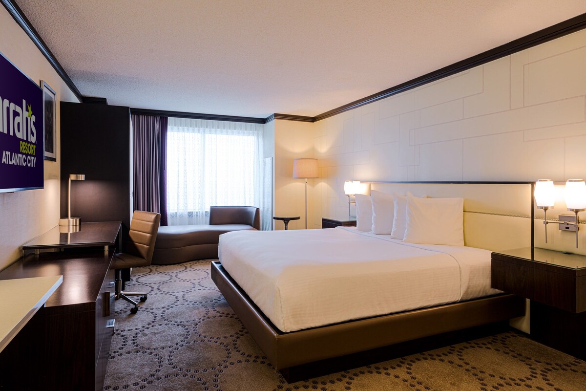 Una habitación de hotel con una cama grande, un escritorio, una silla, una lámpara y un letrero de Harrah's.