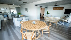 A modern kitchen with stainless steel appliances, a dining area with a round wooden table and wicker chairs, and a living area with wicker sofas and a flat-screen TV. - Romantic Beachfront Cottage 🐕 💙 (Norfolk)