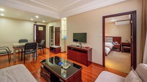 A hotel room with a wooden floor, a TV on a stand, a desk with a chair, a bed, and a door leading to another room. - Yi Feng Bussiness Hotel (Anning)
