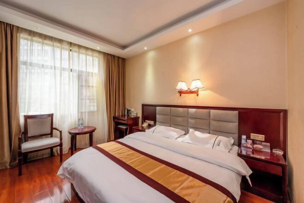 Una habitación de hotel con una cama grande, una silla, una mesita y una mesita de noche con lámpara.