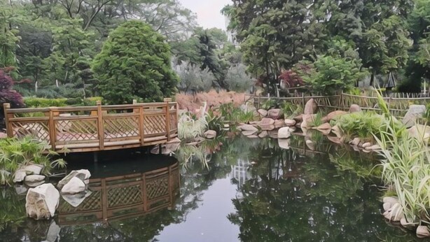 A tranquil pond with a wooden bridge, surrounded by lush greenery and rocks. - Yi Feng Bussiness Hotel (Anning)