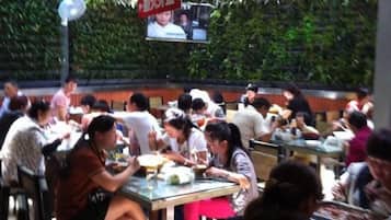 A crowded outdoor dining area with tables and chairs, surrounded by greenery.