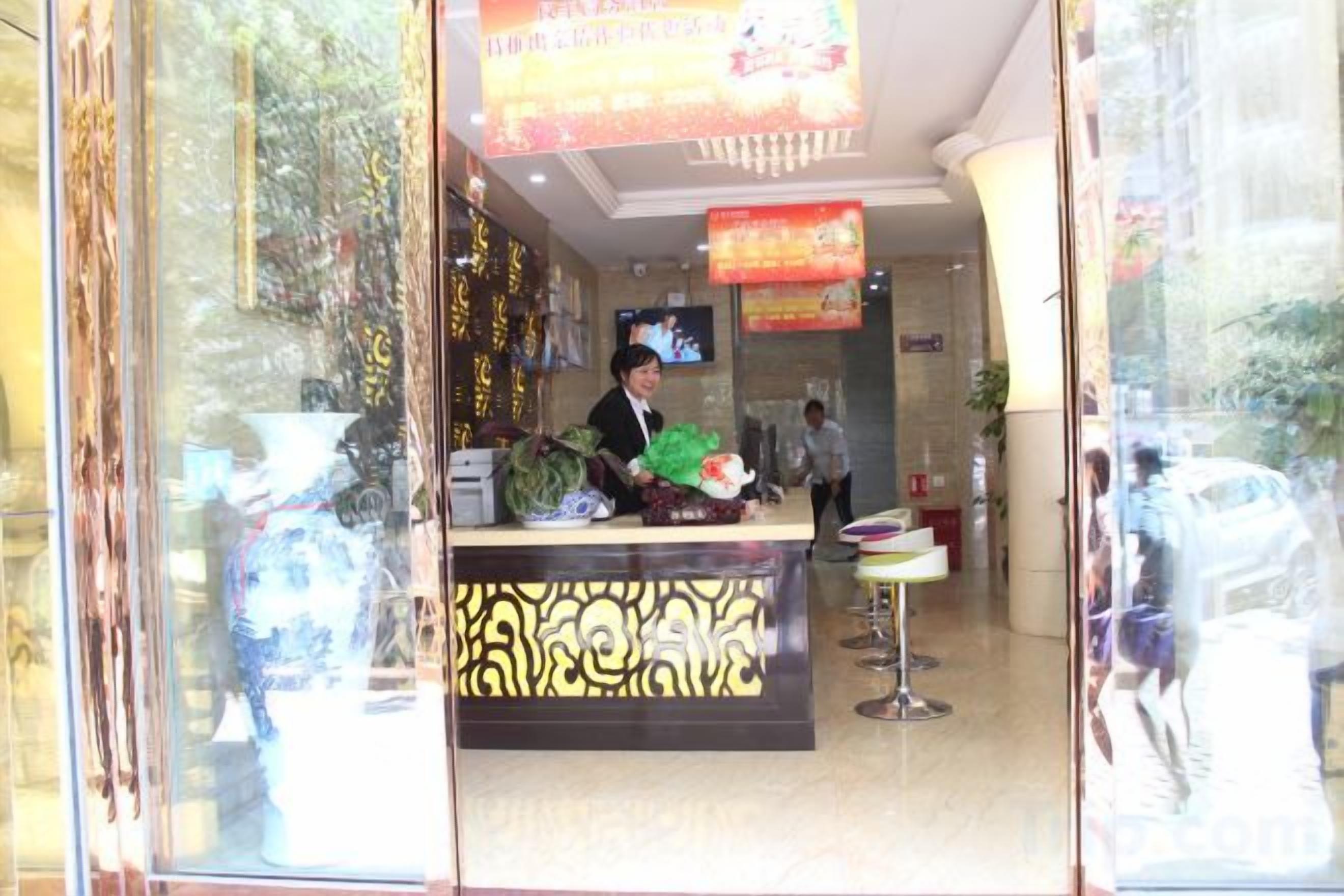 A reception area with a counter, a television screen, and a person seated behind it.