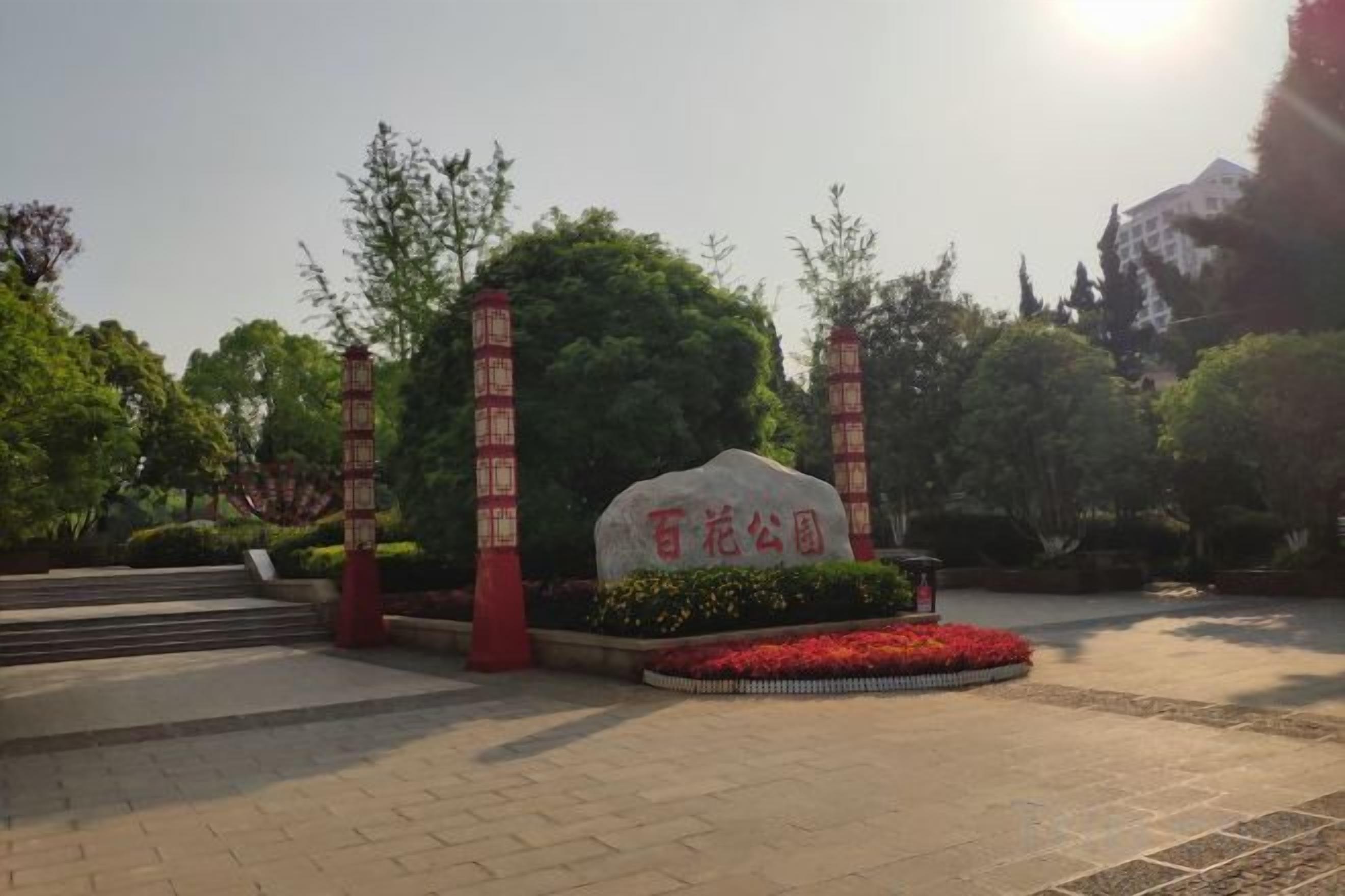 Zona ajardinada con un monumento de piedra, faroles rojos y un parterre circular.