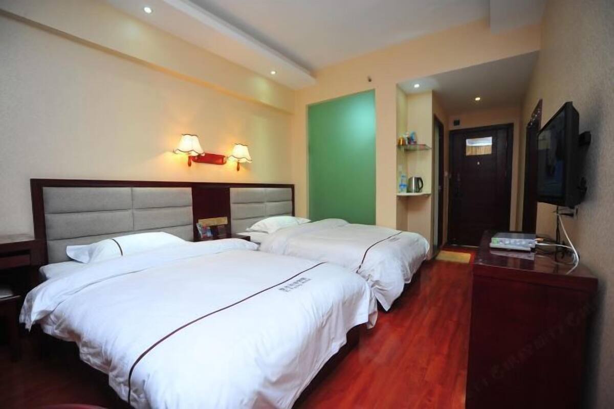 Habitación de hotel con dos camas, cabecero de madera, televisor y una pared de acento verde.