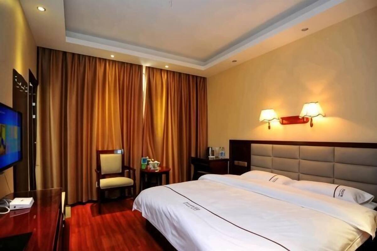 Una habitación de hotel con una cama grande, televisión, una silla, escritorio y dos lámparas de pared.