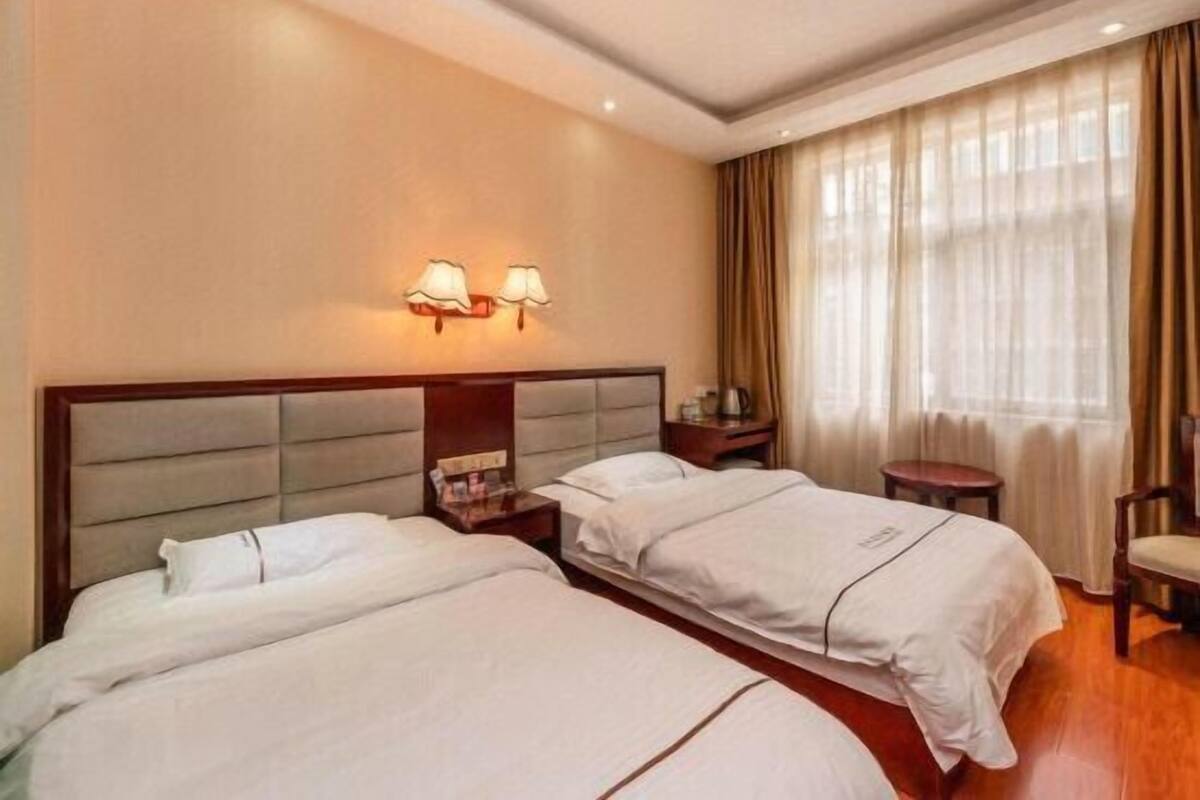 Una habitación de hotel con dos camas, una mesita de noche, una silla y una ventana con cortinas.