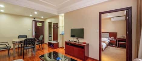 A hotel room with a wooden floor, a flat-screen TV, a desk with a chair, a bed, and a small seating area with a sofa and a coffee table.