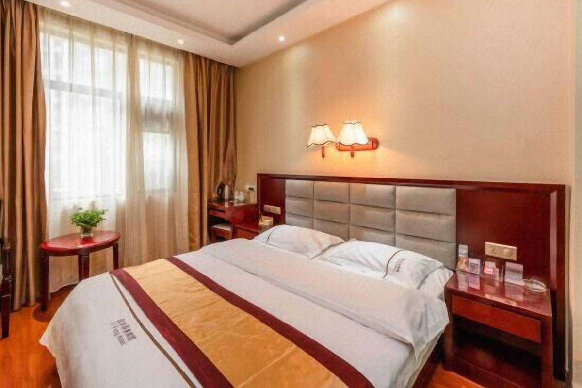 Una habitación de hotel con una cama, una mesita de noche, una lámpara y una ventana con cortinas.