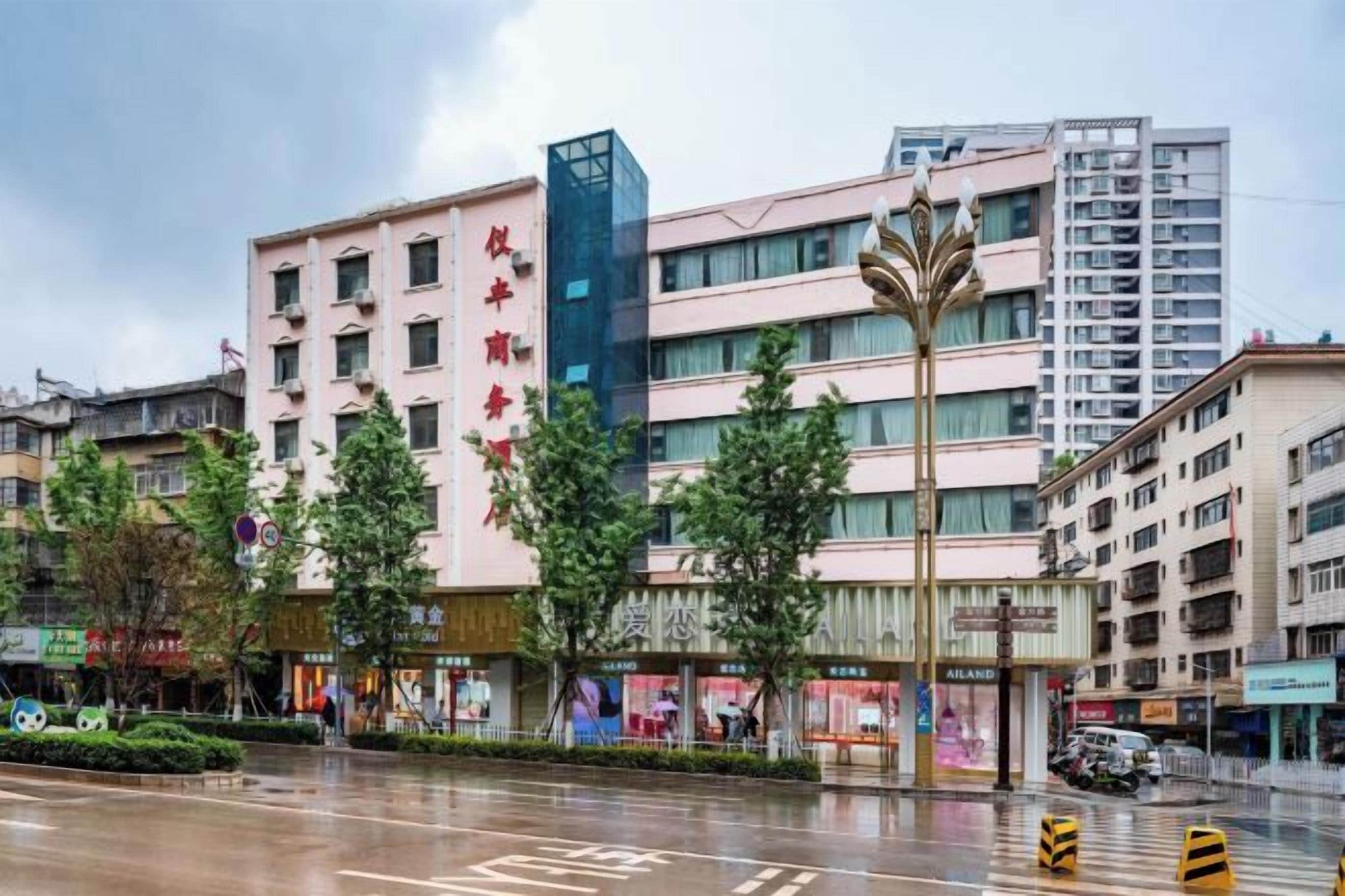 Un hôtel à plusieurs étages, doté d’une façade imposante, d’un parking et situé sur une rue dont la chaussée est mouillée.