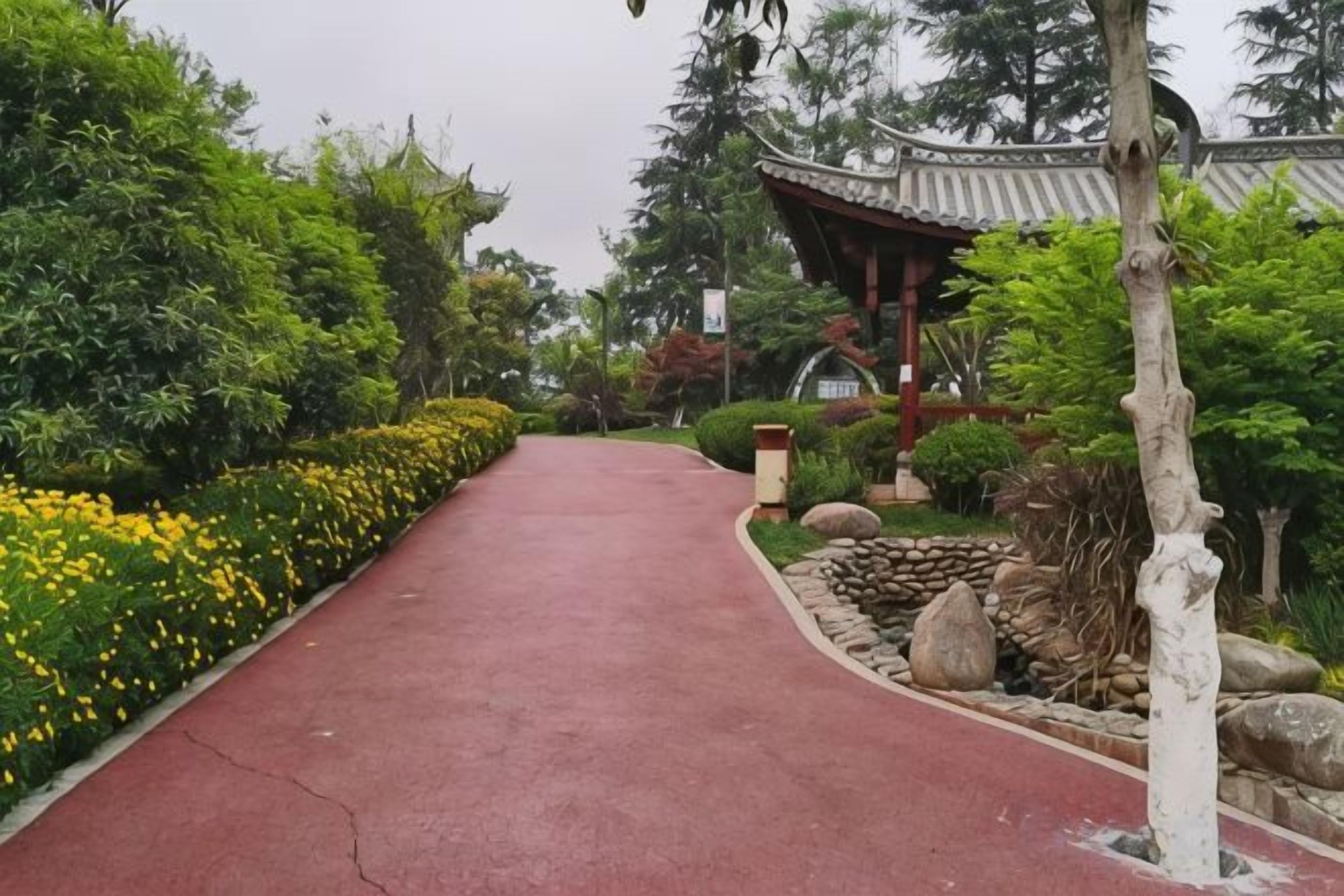 A pathway leading to a traditional-style building with a tiled roof, surrounded by lush greenery and yellow flowers.