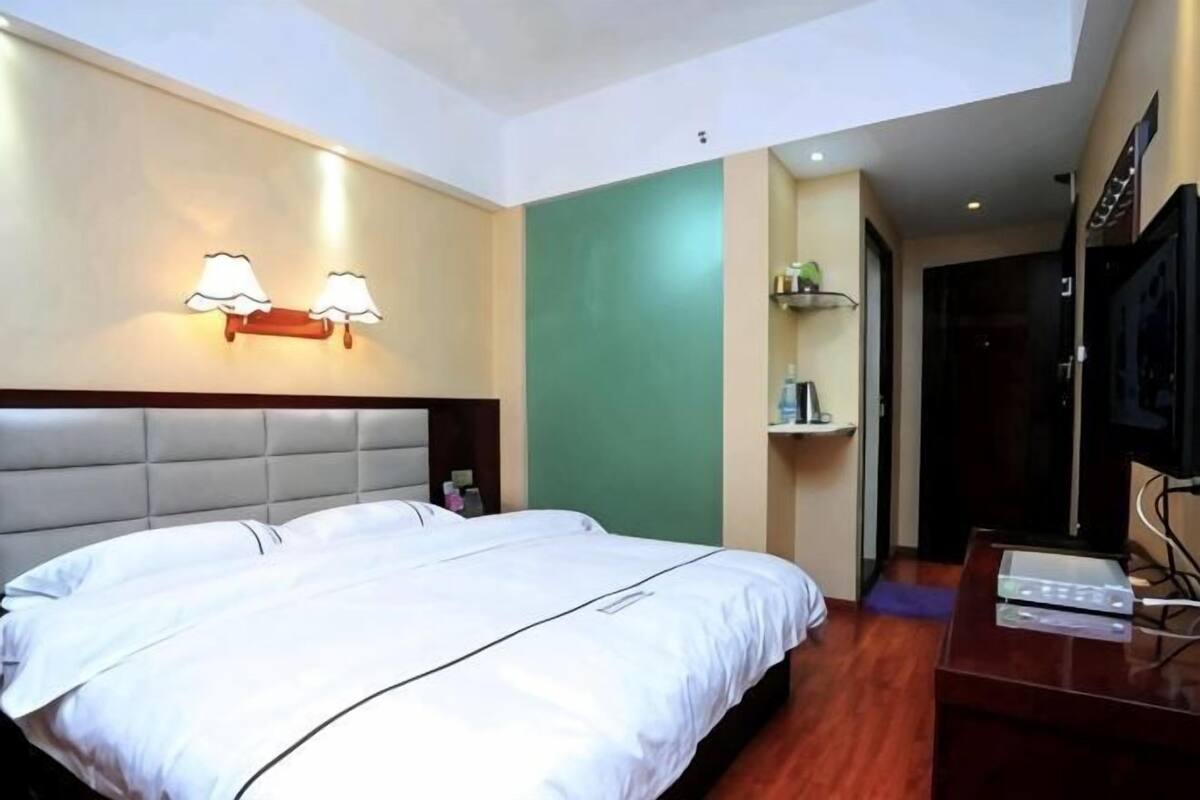 Habitación de hotel con una cama grande, cabecera, lámpara de pared, televisor y suelo de madera.