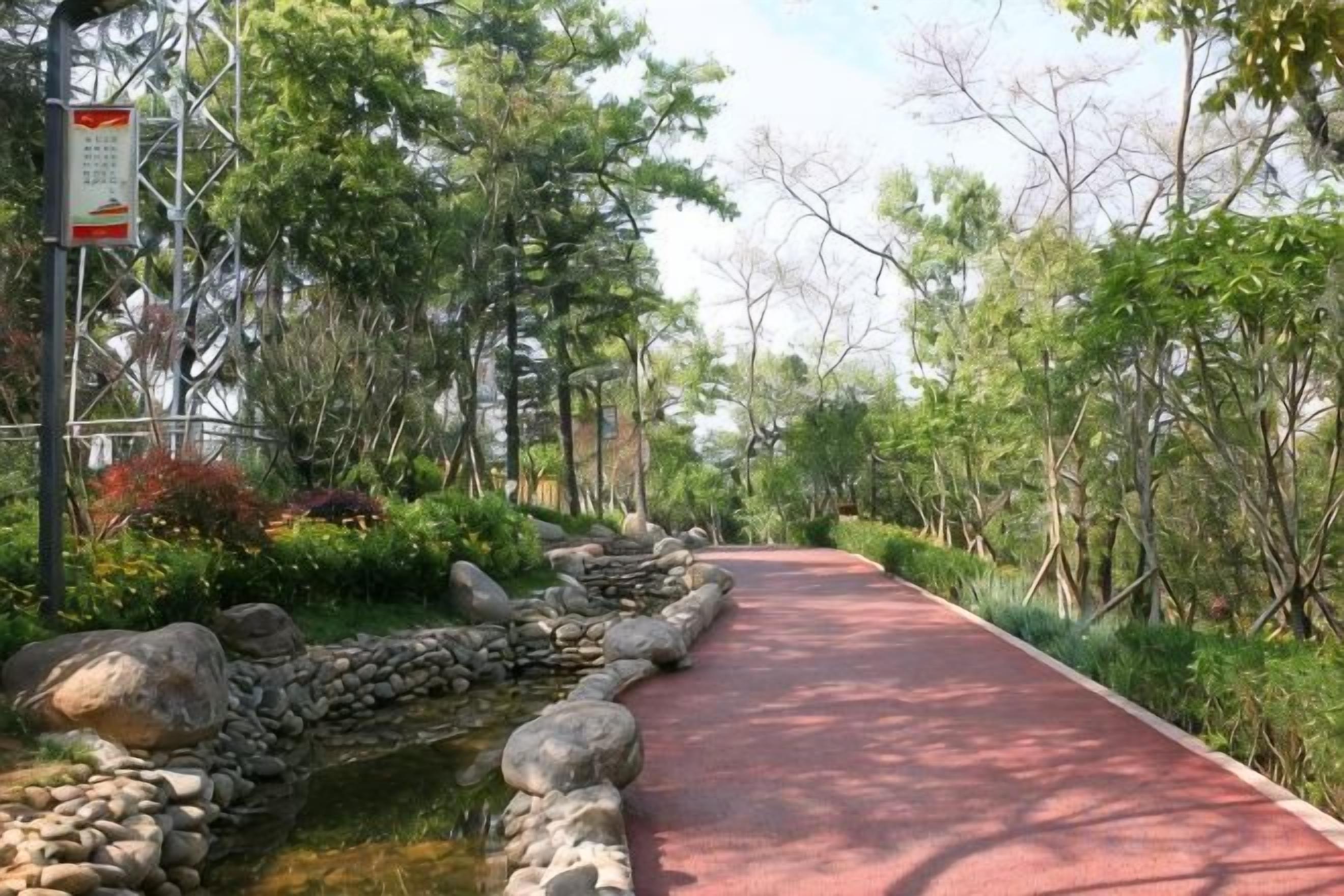 Un sendero bordeado de rocas y follaje, que conduce a una zona pavimentada en rojo.