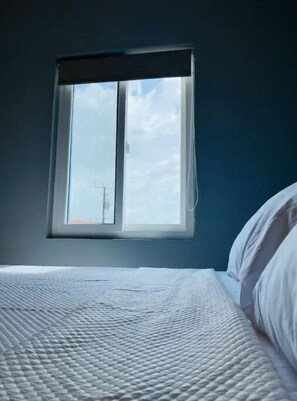 Relax in a cozy room with a single bed, white bedding, and a window offering a view of the sky.