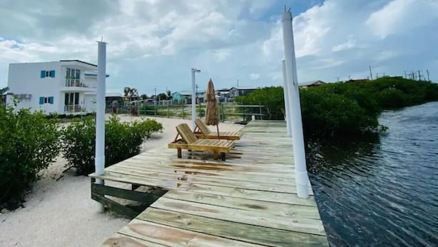 Een houten steiger die zich uitstrekt over een wateroppervlak, met een ligstoel en parasol op het dek.