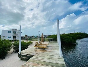 A wooden pier extending into a body of water, with a lounge chair and umbrella on the deck.