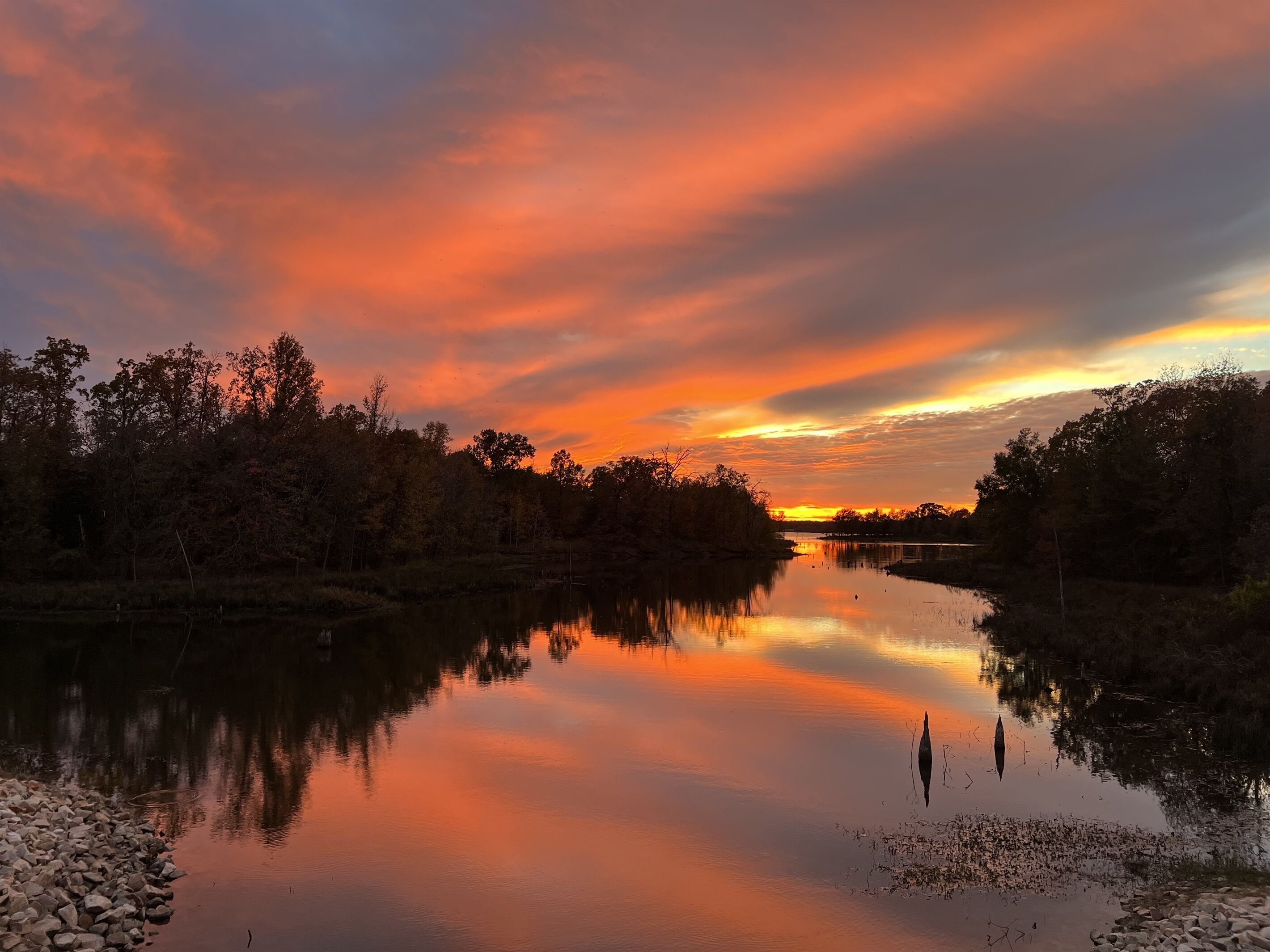 Ein ruhiger Fluss, der einen Sonnenuntergang und Bäume an beiden Ufern widerspiegelt.