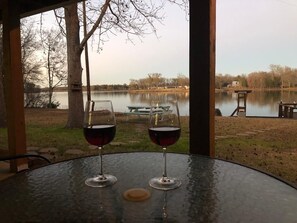 Dos copas de vino sobre una mesa redonda con vistas a un lago y mesas de picnic al fondo.