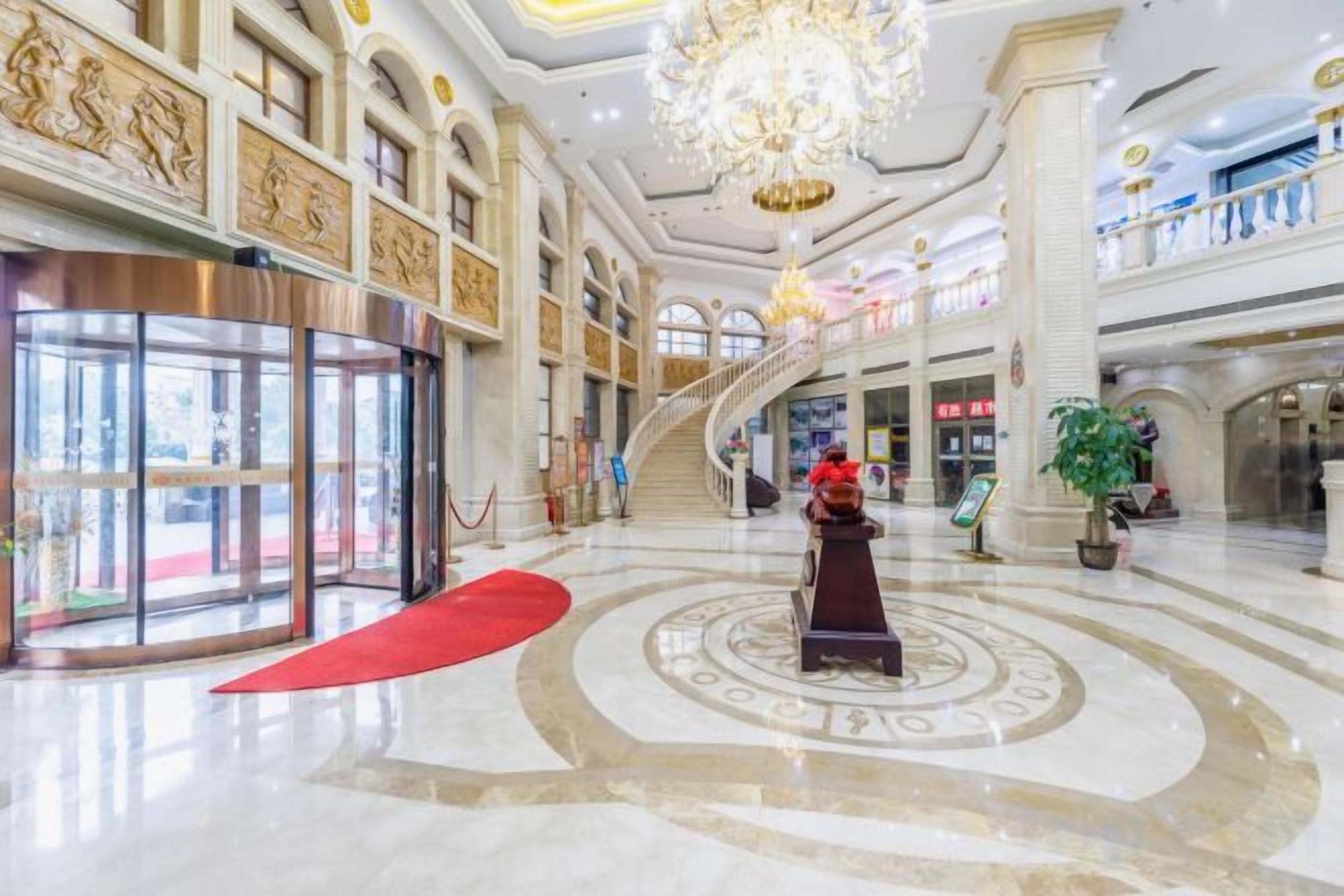 Un hall d’entrée spacieux, agrémenté d’un grand escalier, d’un tapis rouge et d’une statue centrale.