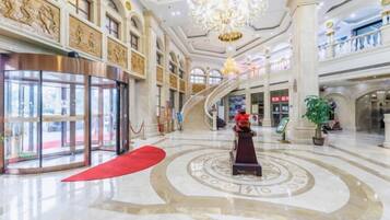 Un hall d’entrée spacieux, agrémenté d’un grand escalier, d’un tapis rouge et d’une statue centrale.