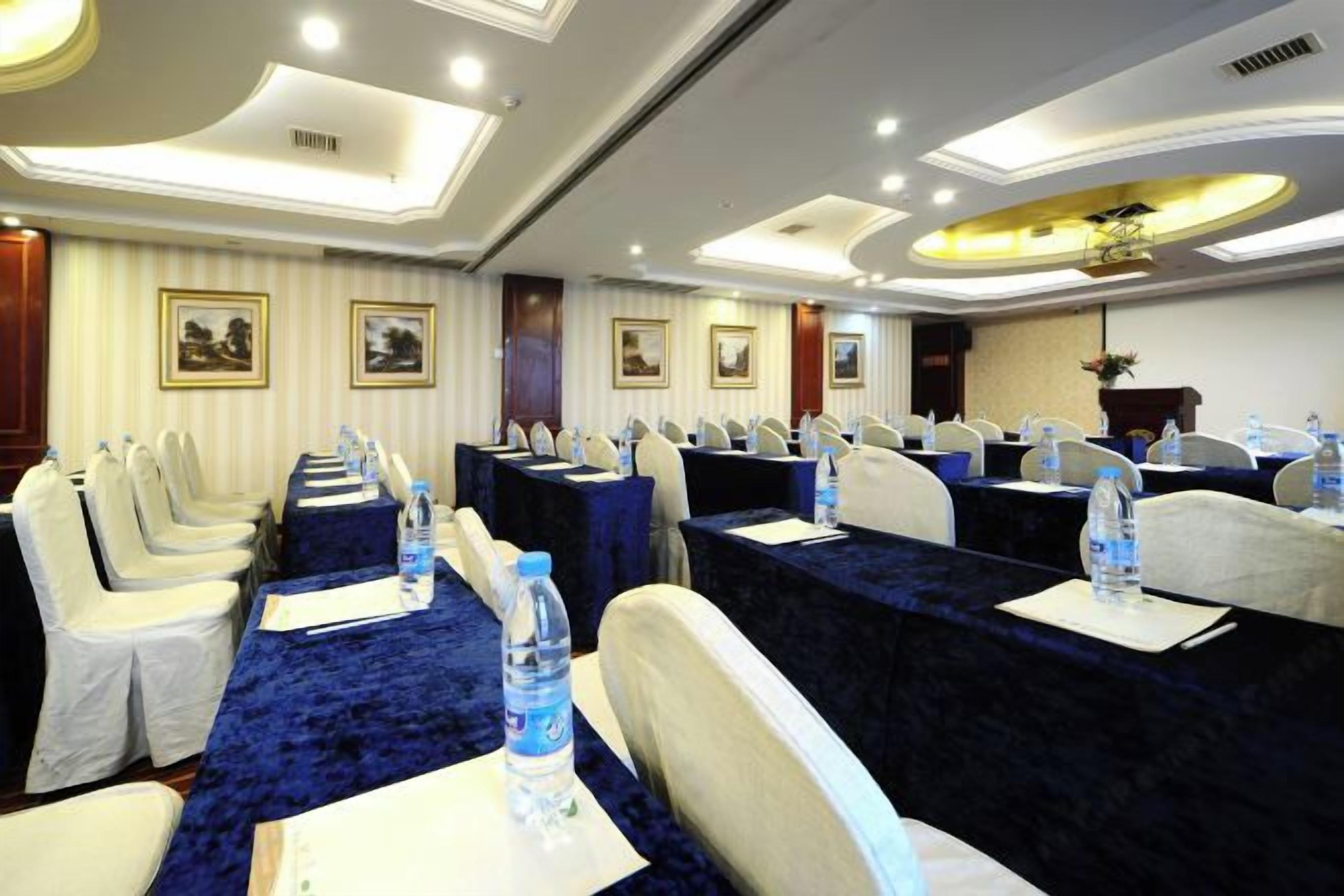 A conference room with rows of tables and chairs, water bottles on each table, and framed pictures on the walls.