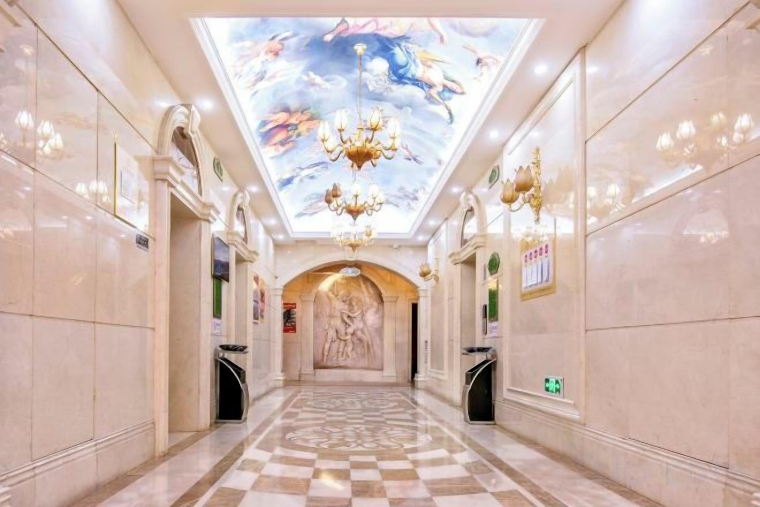 A hotel corridor with a checkered floor, chandeliers, and a mural on the ceiling.