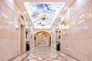 Un pasillo de hotel con piso a cuadros, candelabros y un mural en el techo.