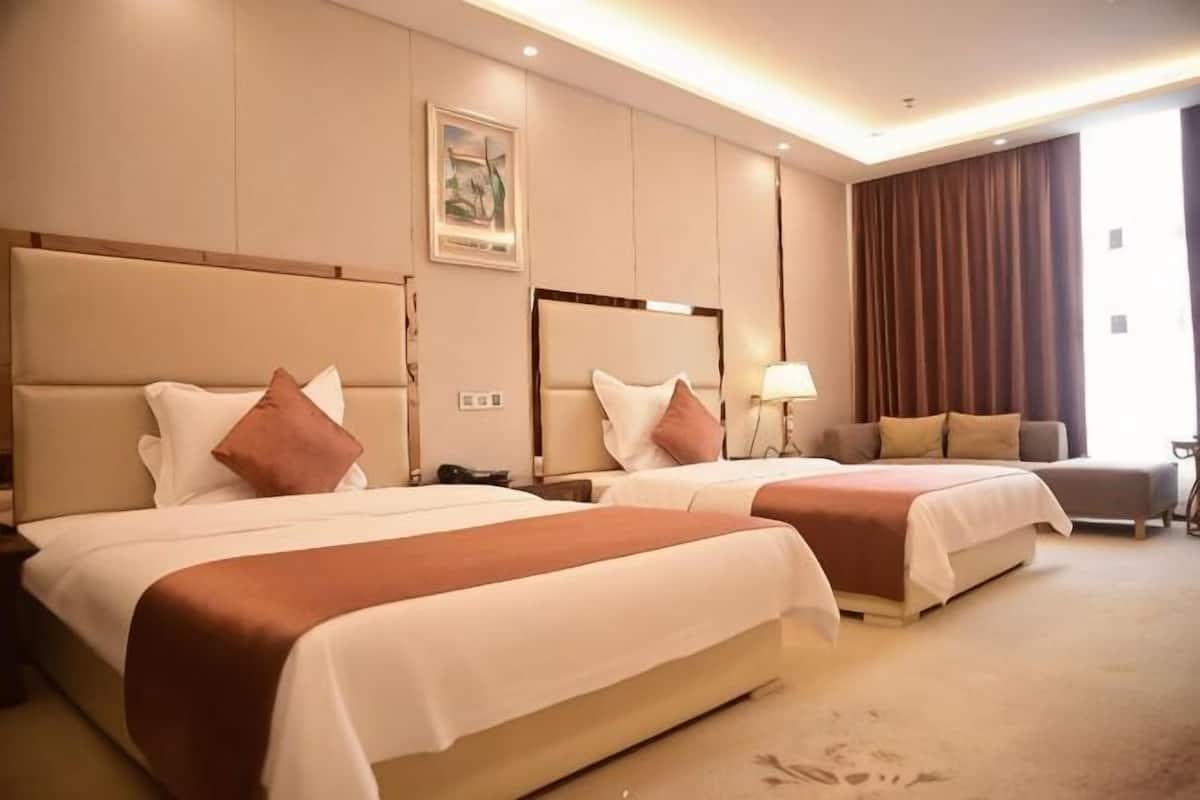 A hotel room with two beds, a nightstand, a lamp, and a large window with curtains.