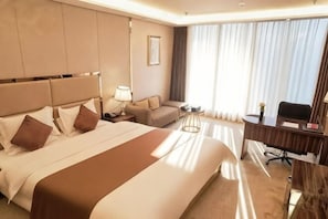 Ein Hotelzimmer mit einem großen Bett, einem Schreibtisch, einem Sessel, einer Couch und einem Fenster mit Vorhängen.