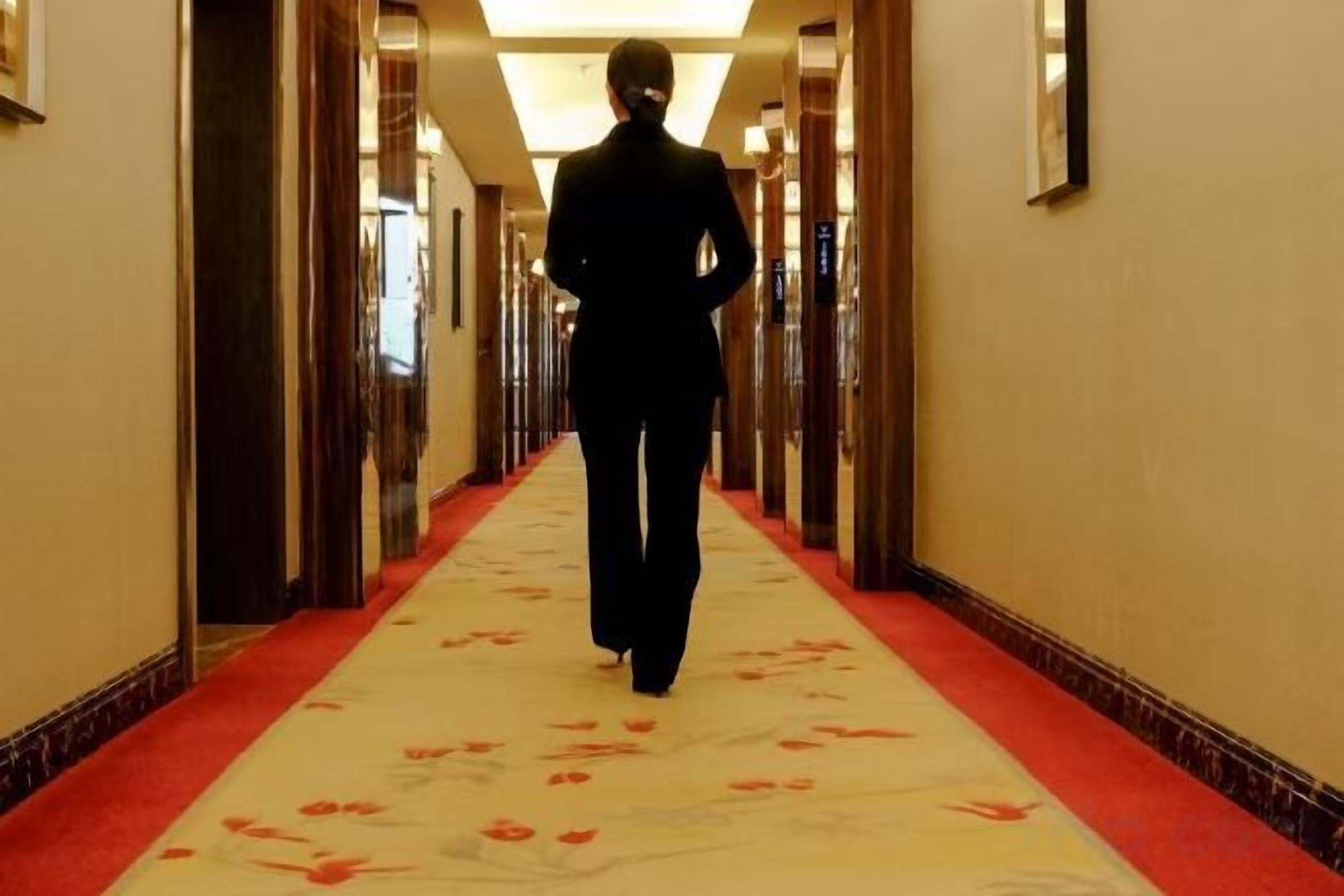 A person walking down a hallway with a red carpet and framed pictures on the walls.