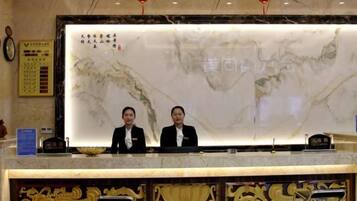 A reception desk with a marble wall and two staff members.