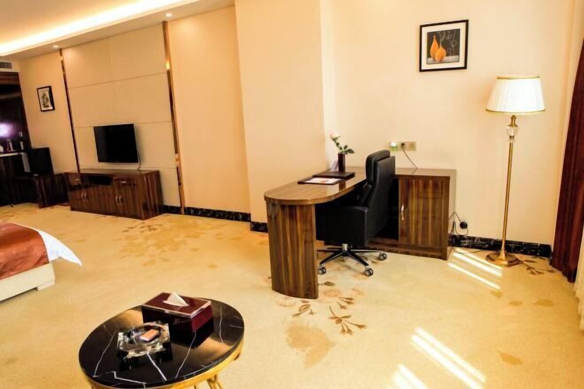 A hotel room with a bed, a desk with a chair, a TV, a lamp, and a carpeted floor.