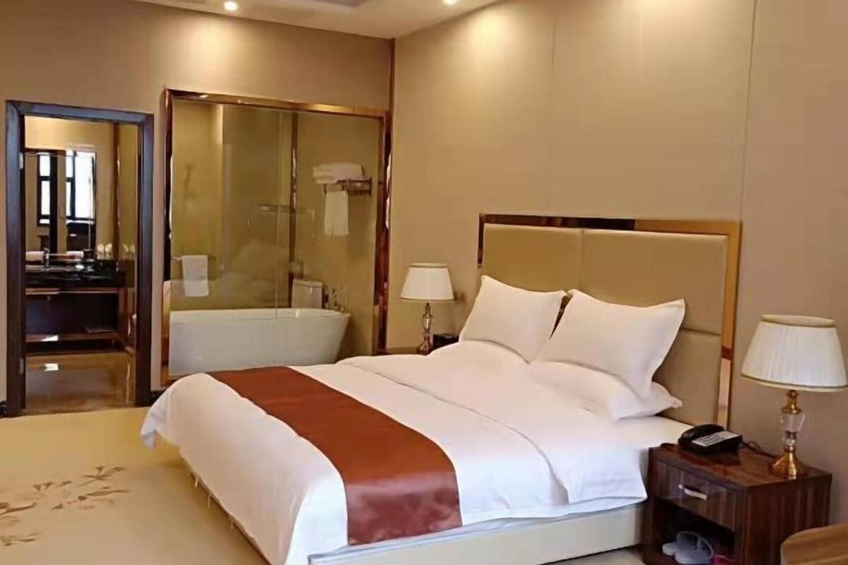 A hotel room with a large bed, a bedside table with a lamp, a mirror, and a bathroom visible through an open door.