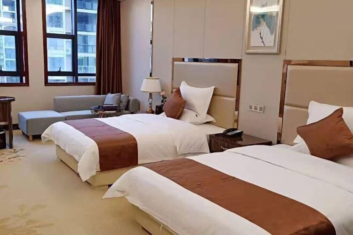 A hotel room with two beds, a sofa, a desk, and a lamp.