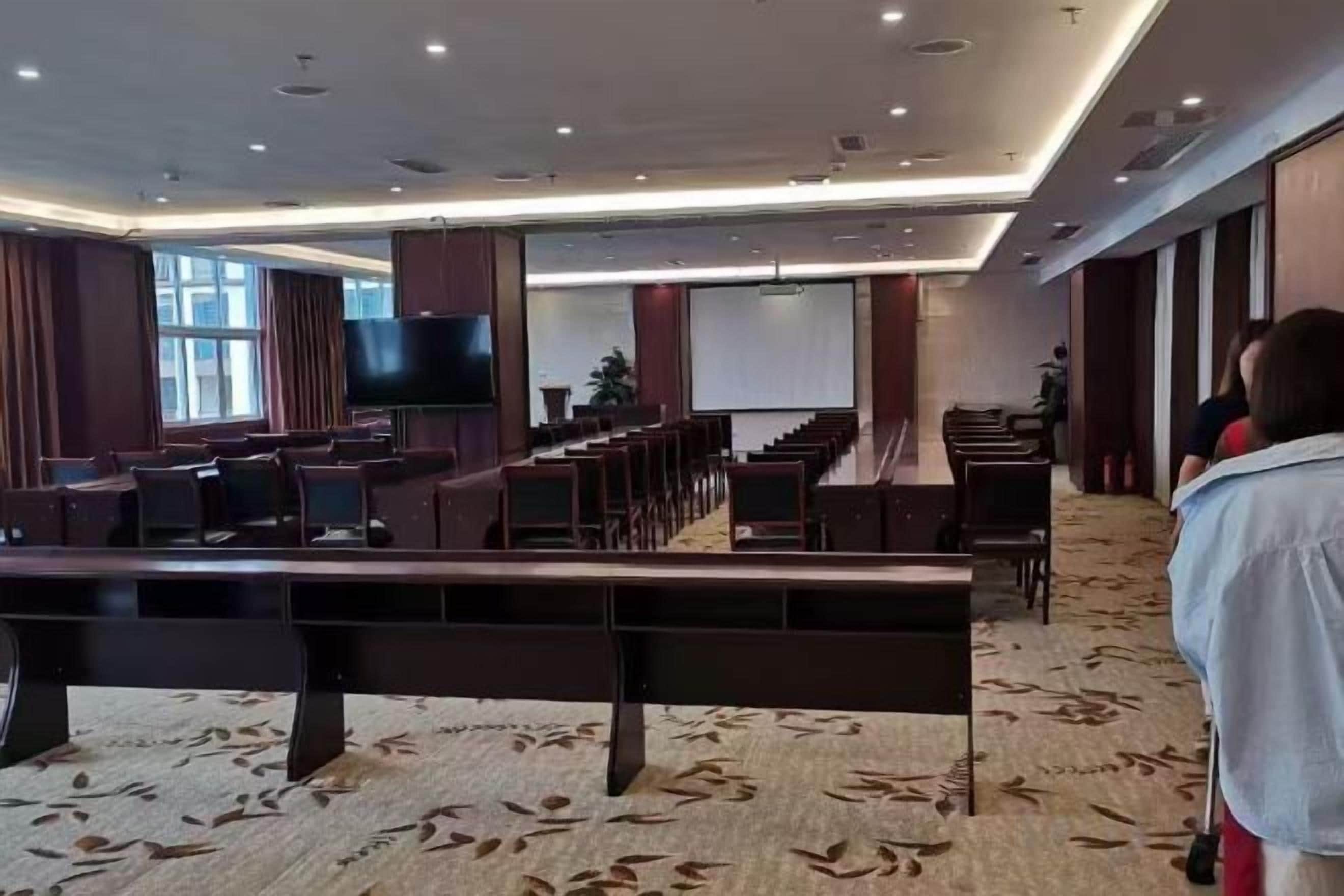 A conference room with rows of chairs, a large screen, and a projection screen.