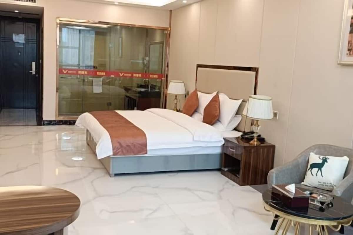 A hotel room with a bed, bedside tables, a chair, and a glass partition.