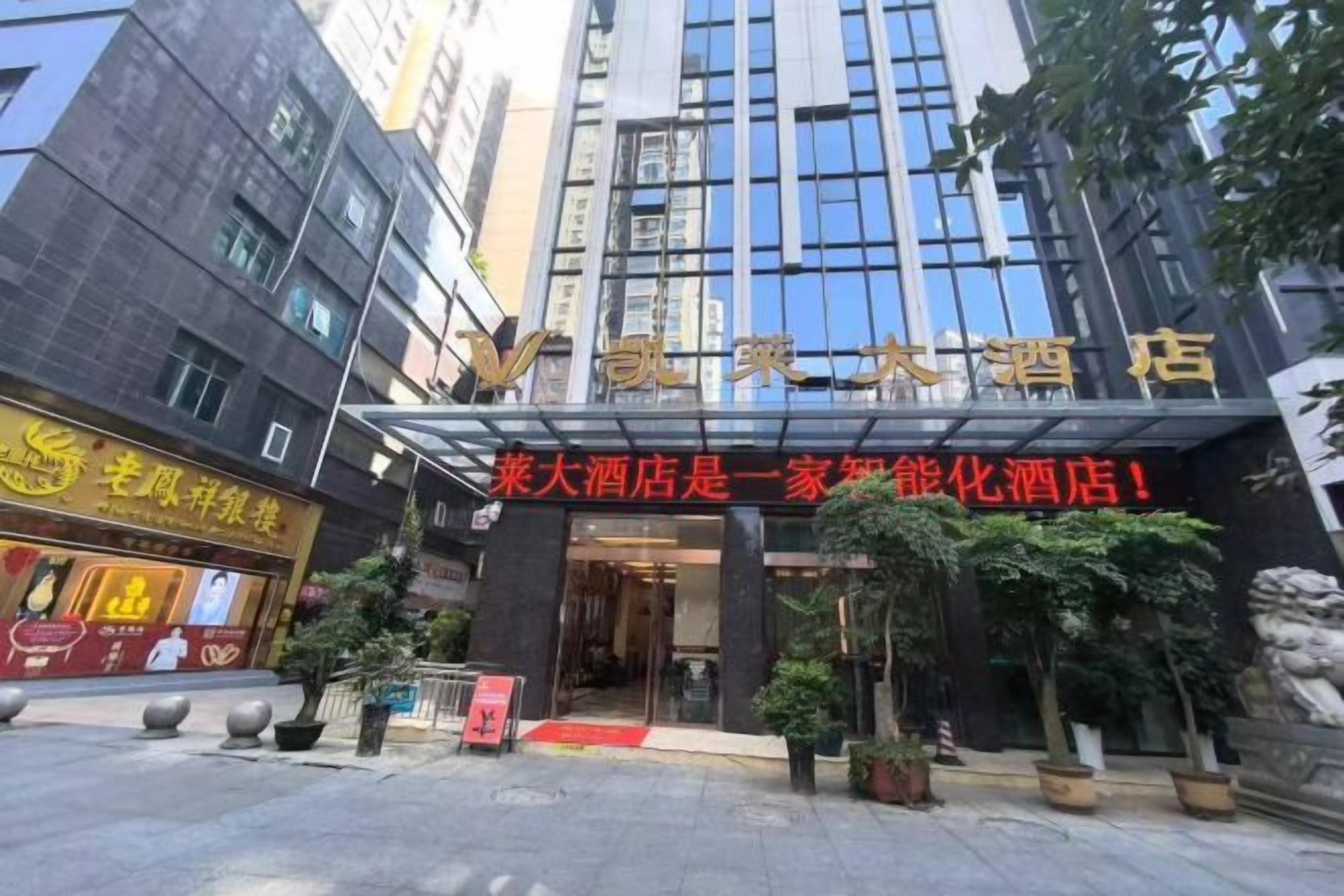 A hotel entrance with a modern facade, a red carpet, and potted plants.