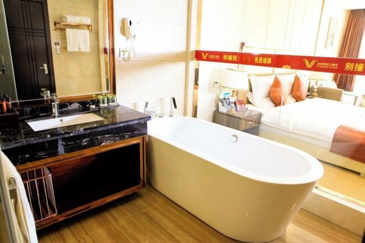 A modern bathroom with a freestanding bathtub, a vanity with a mirror, and a large mirror above the bed.