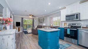 Una cocina moderna con armarios blancos, una isla azul, electrodomésticos de acero inoxidable y un comedor con vistas.