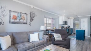Una sala de estar moderna con un sofá gris, una mesa de centro con una planta y una zona de comedor con una isla azul.