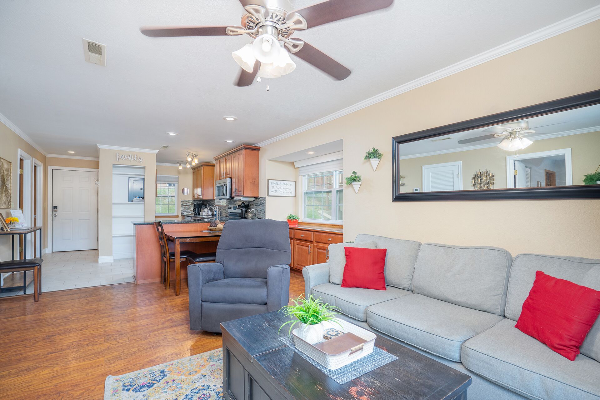 A spacious living room with a grey sofa, a coffee table with a plant, and a ceiling fan.