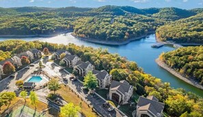 Residential area with a swimming pool surrounded by traditional houses on a hillside, offering views of the surrounding landscape and lush greenery.