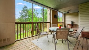 A covered patio with a table and chairs, large windows, and a view of trees.