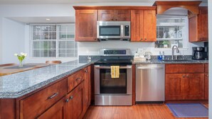 Une cuisine moderne avec des meubles en bois, des appareils en acier inoxydable, des plans de travail en granit et une fenêtre équipée de stores.