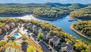 Residential area with a swimming pool surrounded by houses with pitched roofs in a lush, green environment.