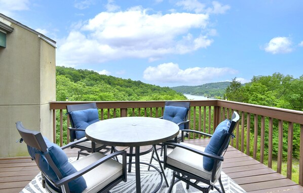 A deck with a round table and four chairs, overlooking a lush green landscape and a body of water.