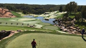 Een golfbaan met bunkers, waterhindernissen en een golfer op de voorgrond.