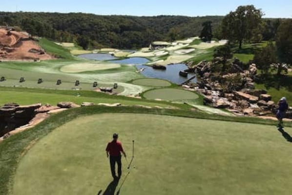 A golf course with bunkers, water hazards, and a player in the foreground.